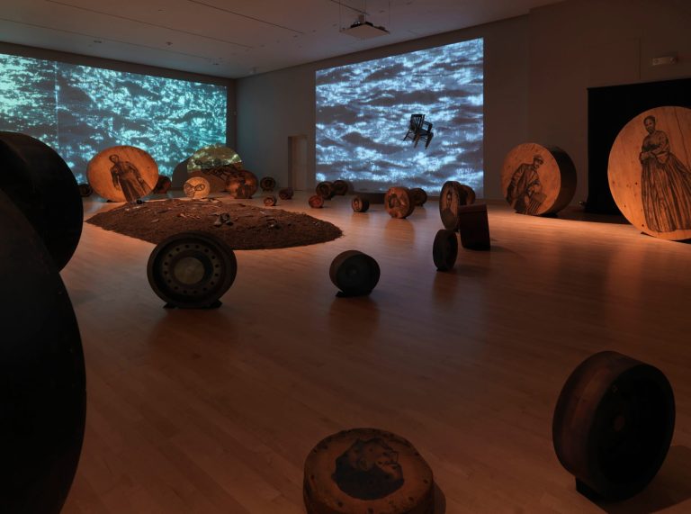 Deep River, 2013 - Fifty-six wooden discs, found objects, soil, video projections, sound. Dimensions variable. Courtesy of American Federation of Arts, the artist, and DC Moore Gallery, New York.